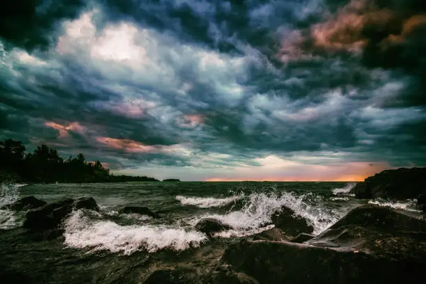 Dramatic sky over Lake Superior in Michigan's Upper Peninsula. Colorful moody sunset as waves crash onto a rocky beach. Dark seascape background with copy space.