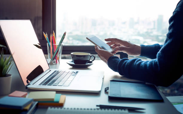 hombre joven con smartphone con obra moderna mesa y ordenador portátil y paisajes urbanos vista de ventana. ideas de conceptos de negocio. análisis de la estrategia - office supply desk business person human age fotografías e imágenes de stock