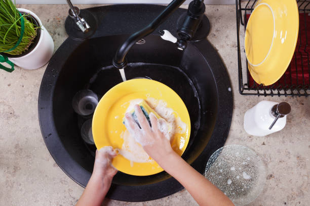 Child hands washing yellow plates at the kitchen sink Child hands washing yellow plates at the kitchen sink - doing the dishes, top view wash dishes stock pictures, royalty-free photos & images