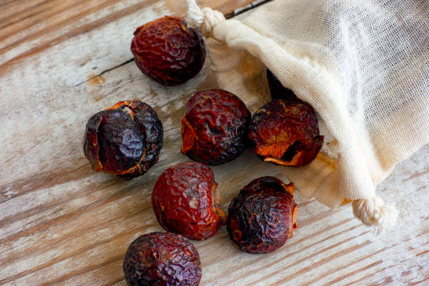 Soap nuts spilling from textile bag on wooden background.
