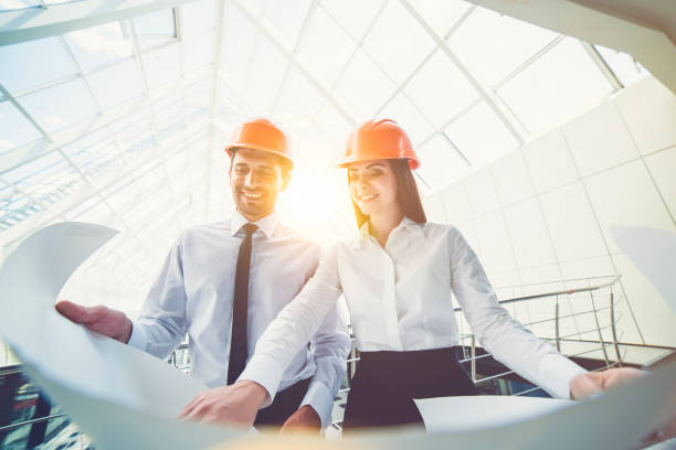 мужчина и женщина в шлемах держат план проекта в здании - architecture businessman construction business стоковые фото и изображения
