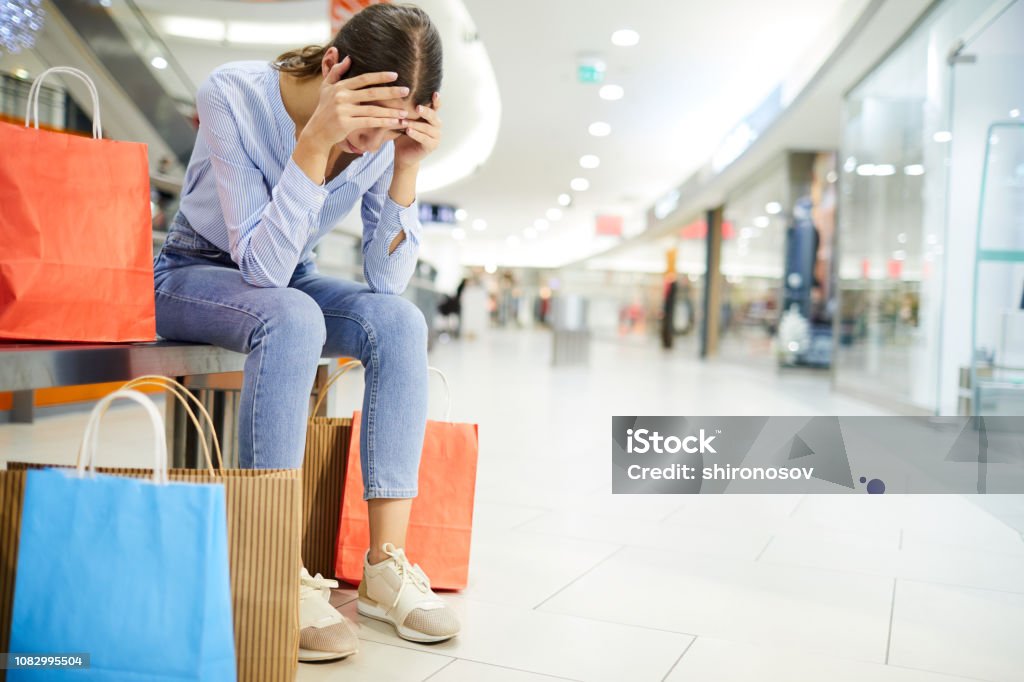 Exhausting shopping Tired shopper holding by head while sitting on bench among paperbags with purchases in the mall Retail Stock Photo