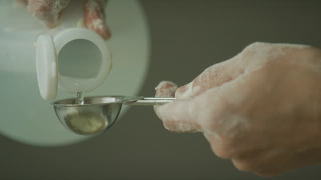 A Young Woman's Hands Use a Small Metal Measuring Spoon to Measure White Vinegar While Baking/Cooking