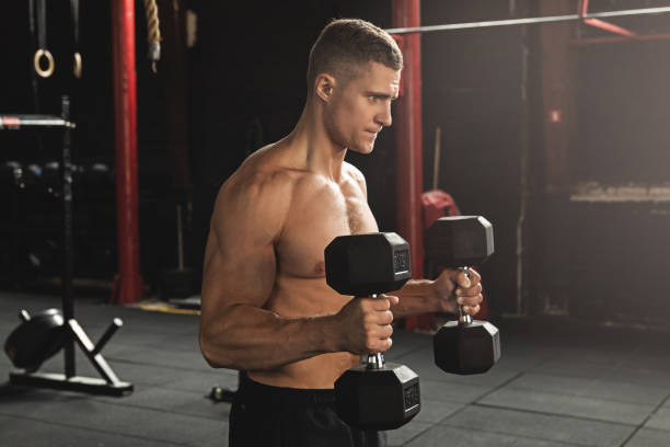 Young handsome bodybuilder during his arm workout in the gym Young handsome bodybuilder working out with dumbbells. Bicep hammer curl exercise. arm hammer stock pictures, royalty-free photos & images