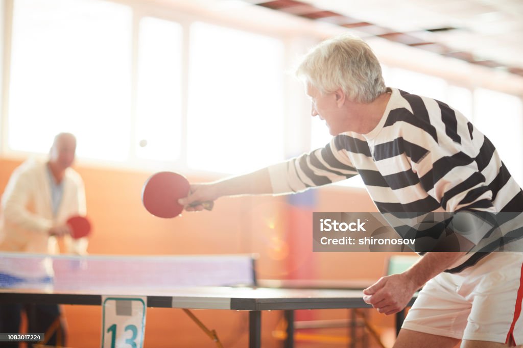Game of ping pong One of ping pong players hitting ball while passing it over table to his mate during game in the hall Table Tennis Stock Photo