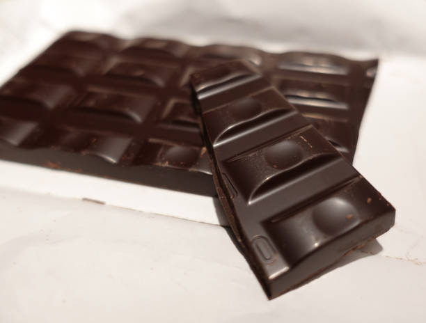 Broken black chocolate bar on white wrapping paper