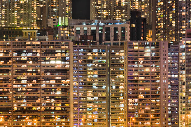 Densely populated skyscraper living towers of houses in Hong Kong at night with bright illumination of windows on island's waterfront.