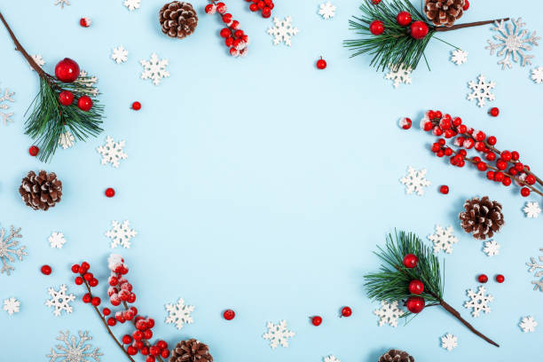 istock Christmas winter frame with icing berries, cones and snowflakes on pastel blue background with place for text in center. View from the top. 1083070440
