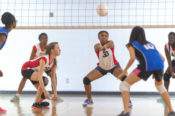 Junior varsity volleyball A volleyball match between high school girl's teams in an indoor gym. The team in red-and-white jerseys are about to bump the ball. volleyball sport stock pictures, royalty-free photos & images