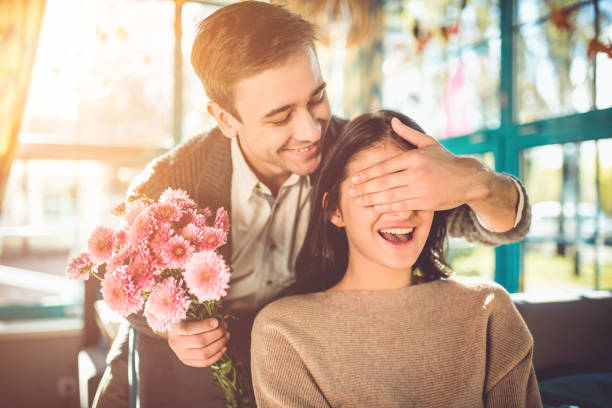 el hombre feliz hacer una sorpresa con flores para una novia en el restaurante - valentine present fotografías e imágenes de stock