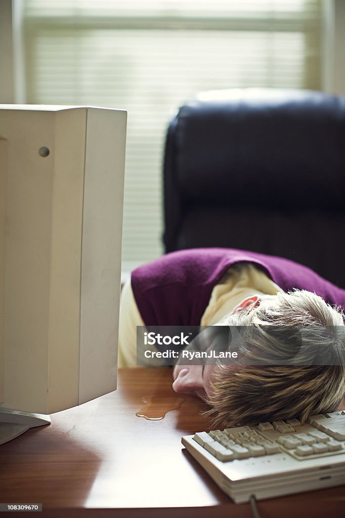 Sleeping Worker Drools In Office An employee at his computer sleeps on his desk, a puddle of drool pouring from his mouth onto the desktop.  Vertical with copy space. Computer Stock Photo