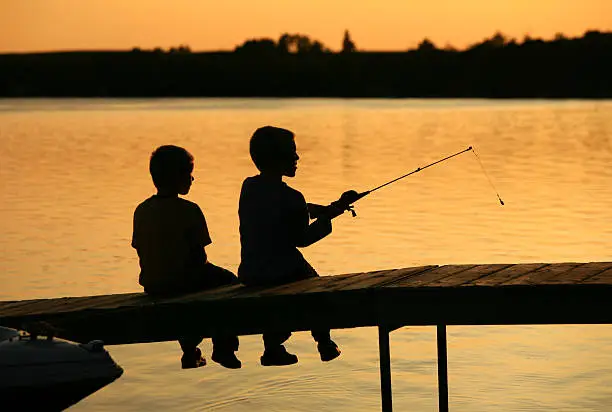 Photo of Silhouette of Two Boys Fishing Off A Dock