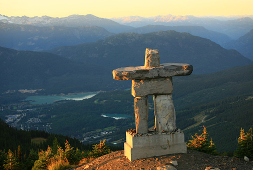 An inukshuk on a mountain peak. Whistler, British Columbia, Canada. The inukshuk is a First nations or aboriginal symbol common in Western Canada. This beautiful inukshuk, or stone statue, sits near the summit of a mountain on the Whistler/Blackcomb ski resort, which is one of the largest in the world. Beautiful sunset sky and low-angled golden light makes this scene pop.  
