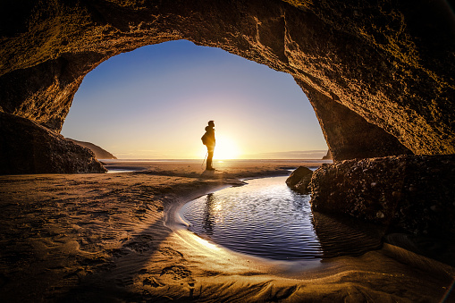 Young man stands at a cave exit. A person deep thinking at the exit of a cave. Beautiful landscape formation of a cave in New Zealand