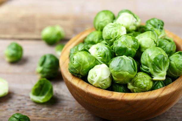 fresca orgánica coles de bruselas crudas en un plato sobre fondo de madera. - col de bruselas fotografías e imágenes de stock