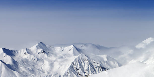 istock Panoramic view on snowy sunlight mountains in haze 1083107356