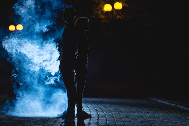 der mann und die frau stehen auf einer dunklen straße auf blauem rauchschwaden. nacht - street fog profile stock-fotos und bilder