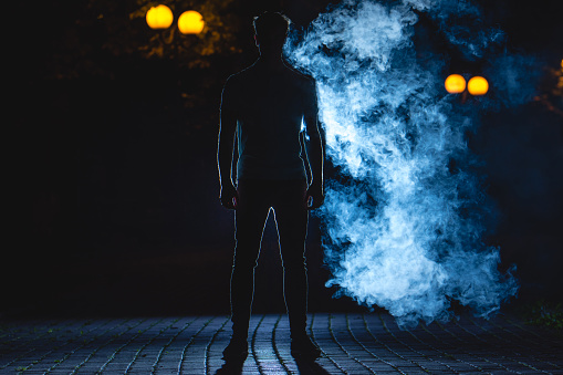 The man stand on the street on a blue smoke background. night time