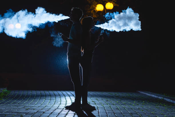 l'uomo e la donna fumano una sigaretta elettrica sulla strada buia. notte - couple dependency standing men foto e immagini stock