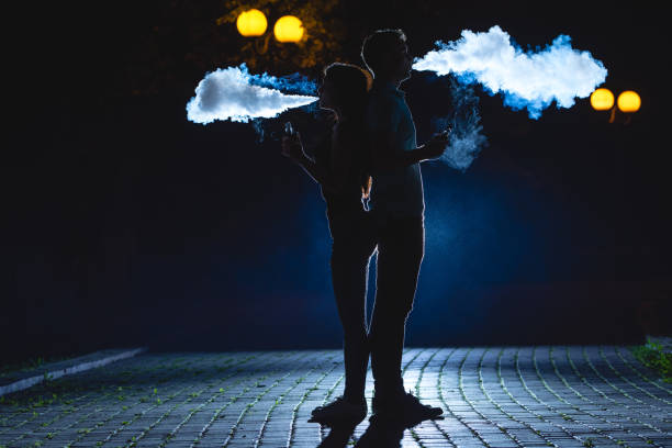 la coppia fuma una sigaretta elettrica sul vicolo buio. notte - couple dependency standing men foto e immagini stock