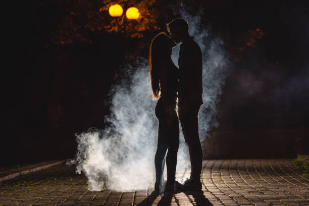 der mann und die frau küssen auf der straße auf einem rauch hintergrund. nachtzeit - street fog profile stock-fotos und bilder