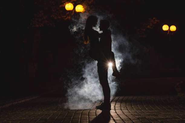 the man lifting a woman on the street with a fume. night time - street fog profile imagens e fotografias de stock