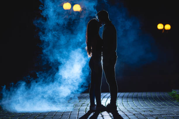das paar küssen auf der straße auf einem blauen hintergrund rauch. nachtzeit - street fog profile stock-fotos und bilder