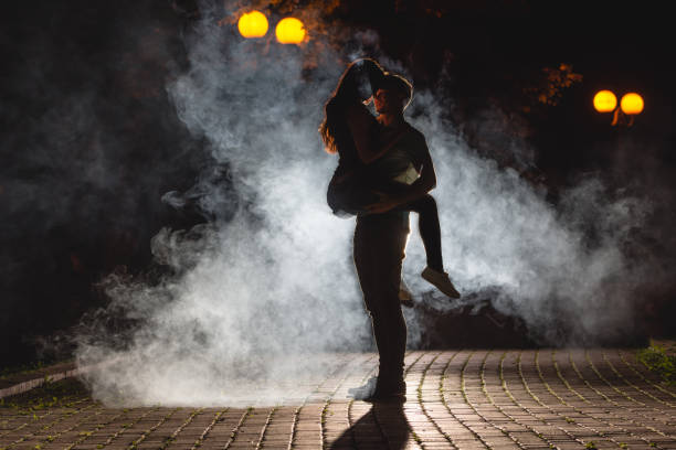 the man lifting a woman on the street with a smoke. night time - street fog profile imagens e fotografias de stock