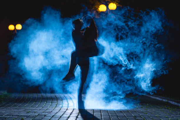 der mann hob eine frau auf der straße mit einem blauen rauch auf. nacht - street fog profile stock-fotos und bilder