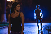 The woman stand on the dark street on the background of the man. night time