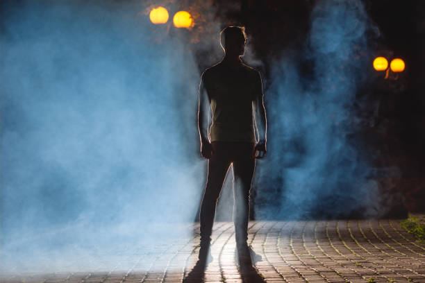 the man stand on the dark street with a fume. night time - street fog profile imagens e fotografias de stock