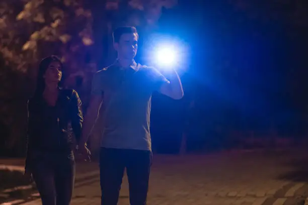 Photo of The man and woman stand with a flashlight on the dark street. night time