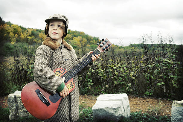 Adorable Little Boy Playing Guitar at Prairie Adorable little boy in vintage hat and jacket plays red guitar at the prairie. rockabilly boys stock pictures, royalty-free photos & images