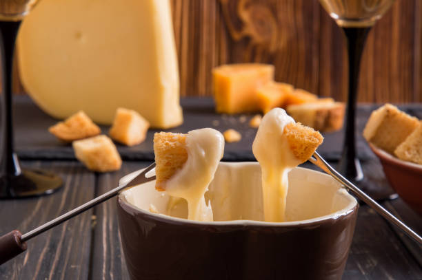 bouchent. dîner gastronomique fondue suisse sur un soir d’hiver avec des fromages assortis sur une planche aux côtés d’une casserole chauffée de fondue au fromage avec deux fourchettes à tremper le pain vin blanc. - fondue swiss culture winter cheese photos et images de collection