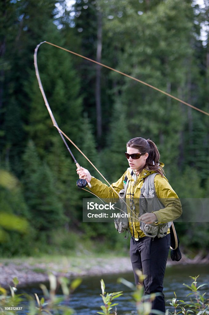 Woman In Yellow Jacket Casting A Fly Rod In Lake Stock Photo
