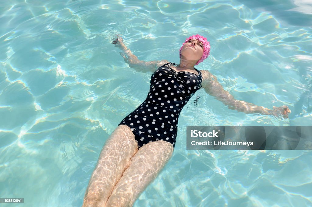 Retro Woman Swimming In Beautiful Blue-Green Pool Pretty retro woman in pink flowered swim cap and retro navy and white polka dotted swim suit floating in a sea of beautiful sea green water.  Copy Space.   "Glow" at 15% added for softening effect. Retro Style Stock Photo