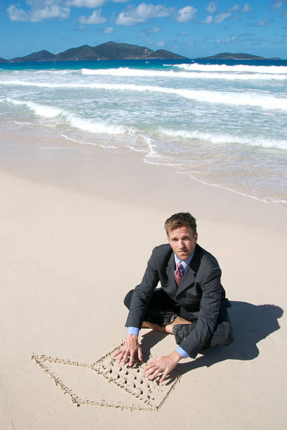 uomo d'affari seduto sulla spiaggia con sabbia digitando portatile - stranded beached beach businessman foto e immagini stock