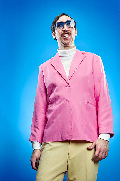 A funny looking salesman with a mustache, blue tinted glasses and a pink blazer with a sickeningly silly grin on his face.  Vertical on teal blue background. 