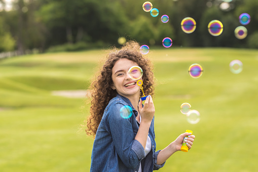 The cheerful woman blowing bubbles in the park
