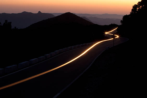 Car headlights trace a winding path through the dark as the last light of the sunset fades into the Sierra Betica mountain range in Andalucia,  Spain.