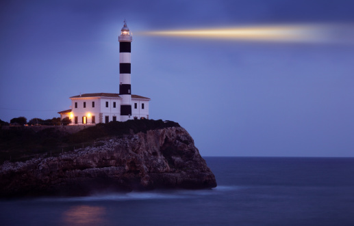 The Punta Nariga Lighthouse on the cliff under the sunrays piercing through the cloudy sky in Spain