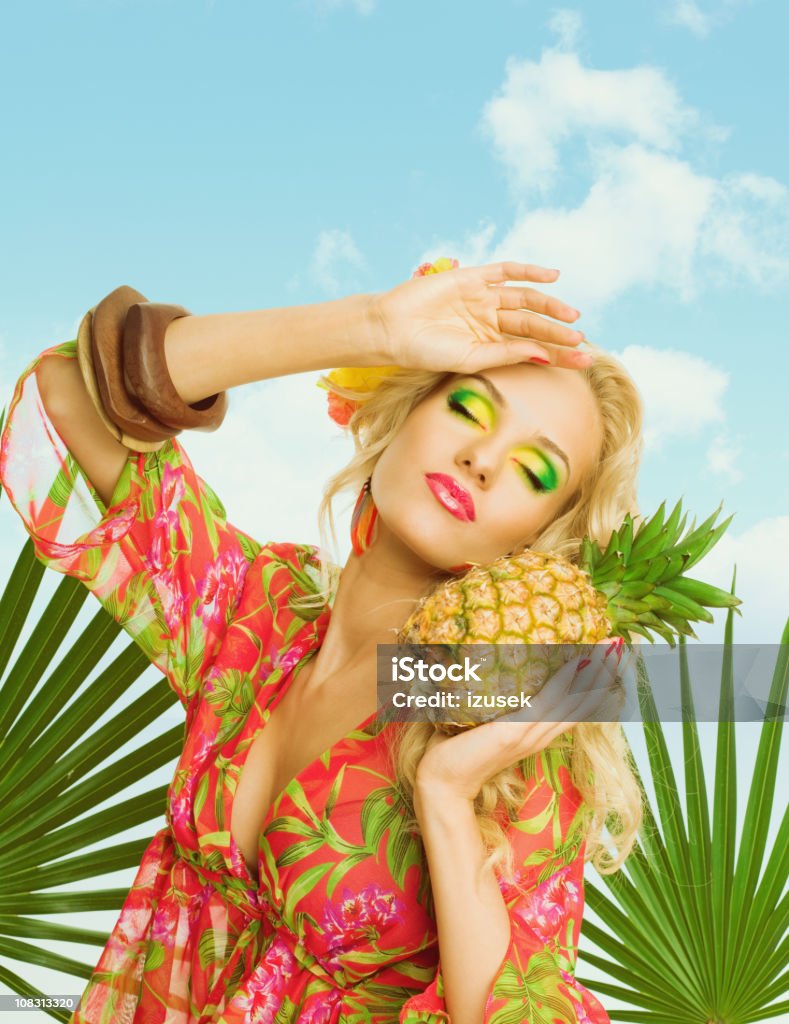 Summer portrait of attractive blonde woman holding pineapple fruit Summer portrait of a beautiful blonde woman wearing a colorful tunic and holding pineapple fruit. Cut Out Stock Photo