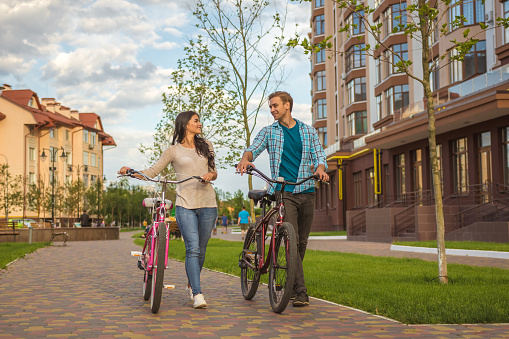 The man and woman walking with a bicycles near modern building