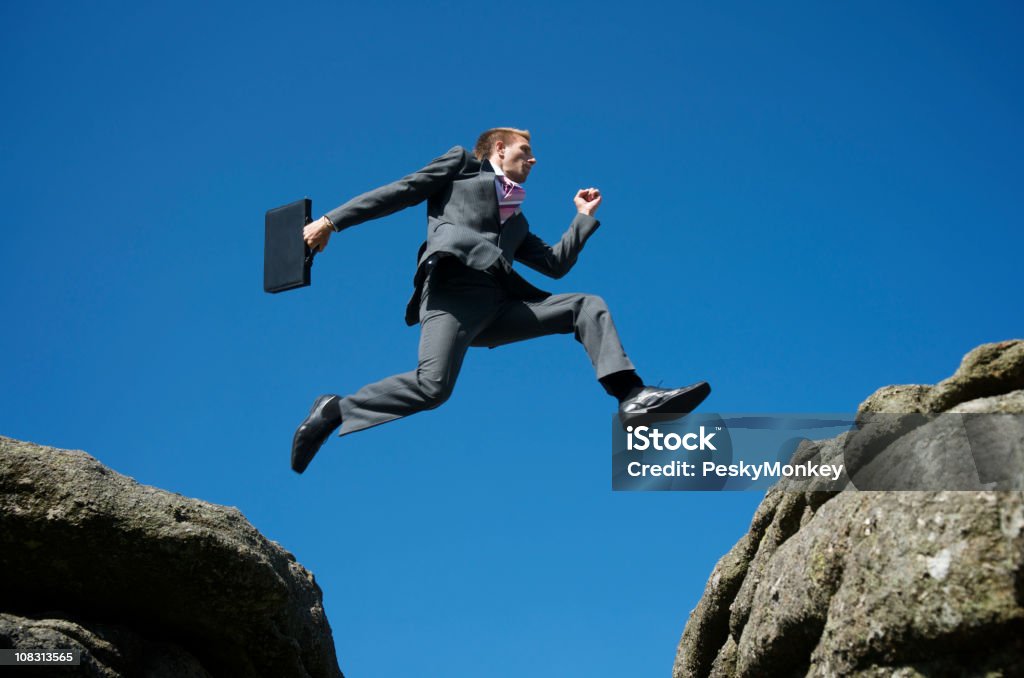 Courageux Homme d'affaires sauter entre Rocks contre ciel bleu - Photo de Affaires libre de droits