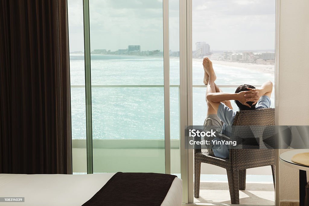 Hombre relajante, con balcón y vista al mar en playa vacaciones - Foto de stock de Balcón libre de derechos