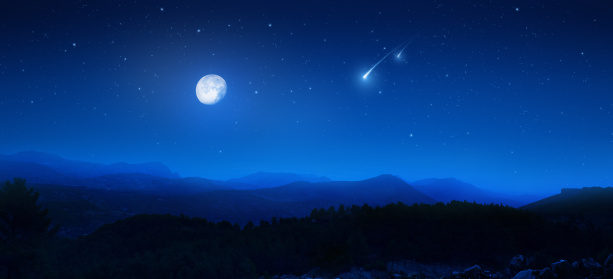 Digital composite view lake with silhouetted trees and mountain seen in moonlight in the Lake District of Cumbria, England.