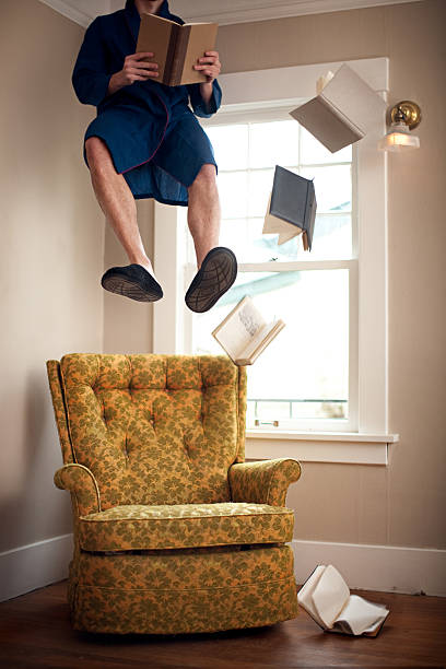 Floating Living Room A man floats suspended in mid air as he reads a book in his living room, surrounded by other floating / falling books.  Vertical with copy space. zero gravity stock pictures, royalty-free photos & images