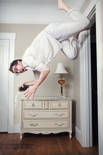 A man in his vintage retro pajamas spills his glass of water as he appears to fall or be suspended in midair in his living room.  Vertical with copy space.