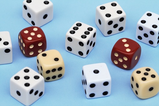 Multiple dice on a blue colored background, Risk, chance or gambling concept. Red, white and off white colored dice in large group. Roll the dice and see what fate gives you.