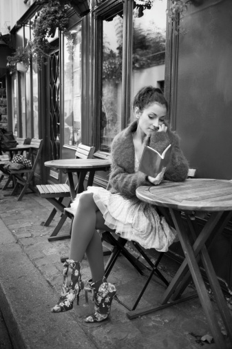 A beautiful Parisian young lady lost in her toughts reading her notebook at a sidewalk cafe in Paris.